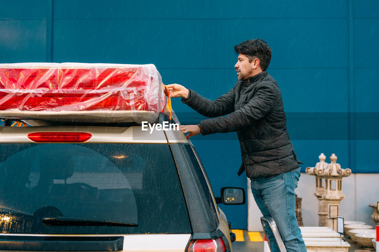 Man securing mattress on car top in a rainy evening