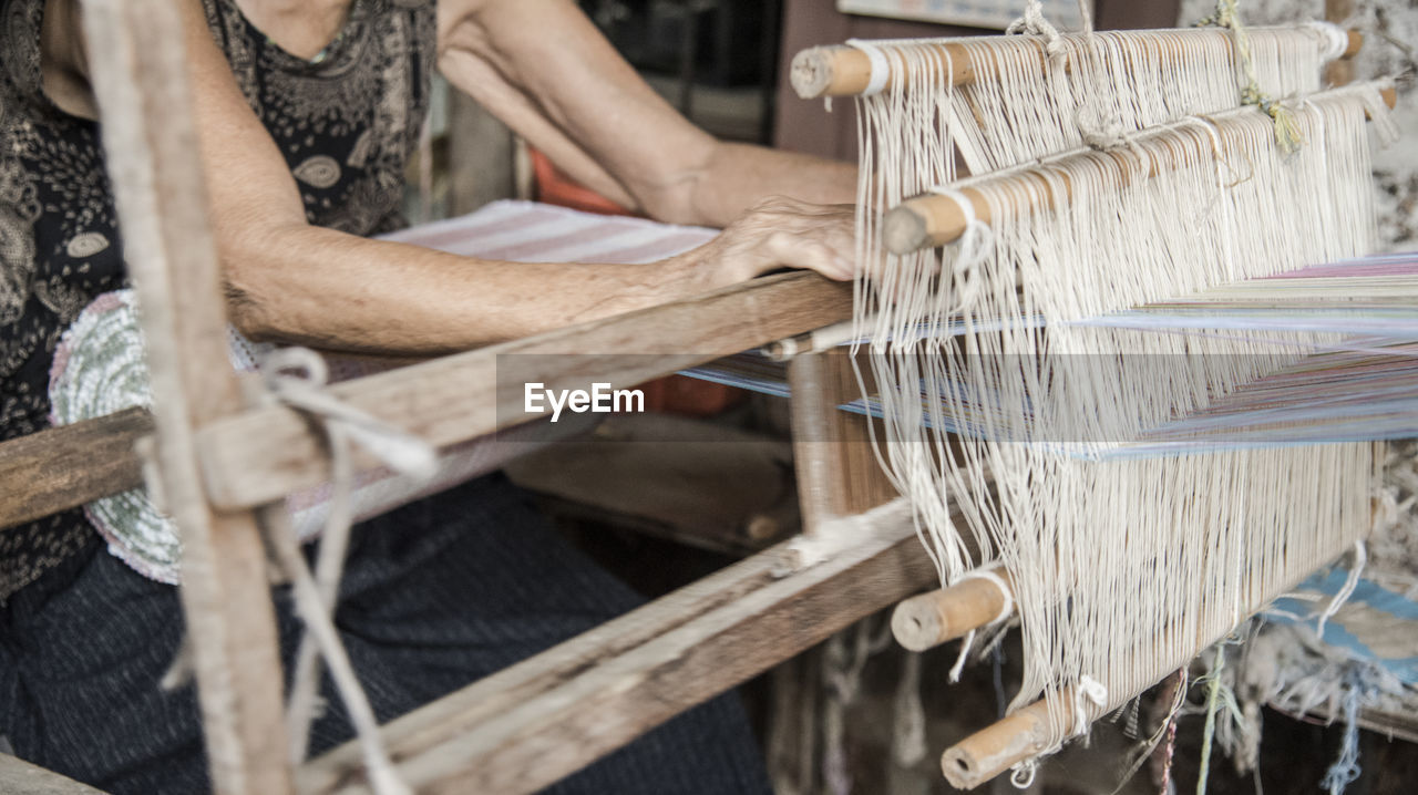 Midsection of woman weaving loom in factory