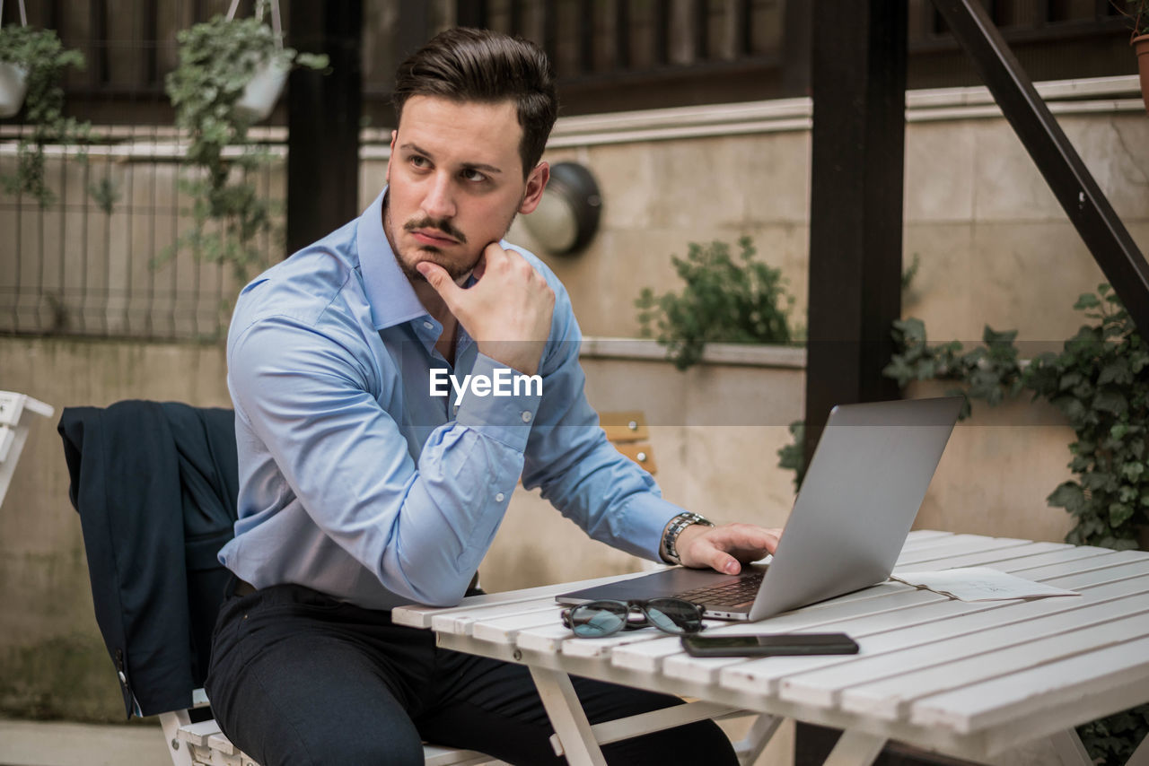 Thoughtful businessman using laptop while sitting on table outdoors