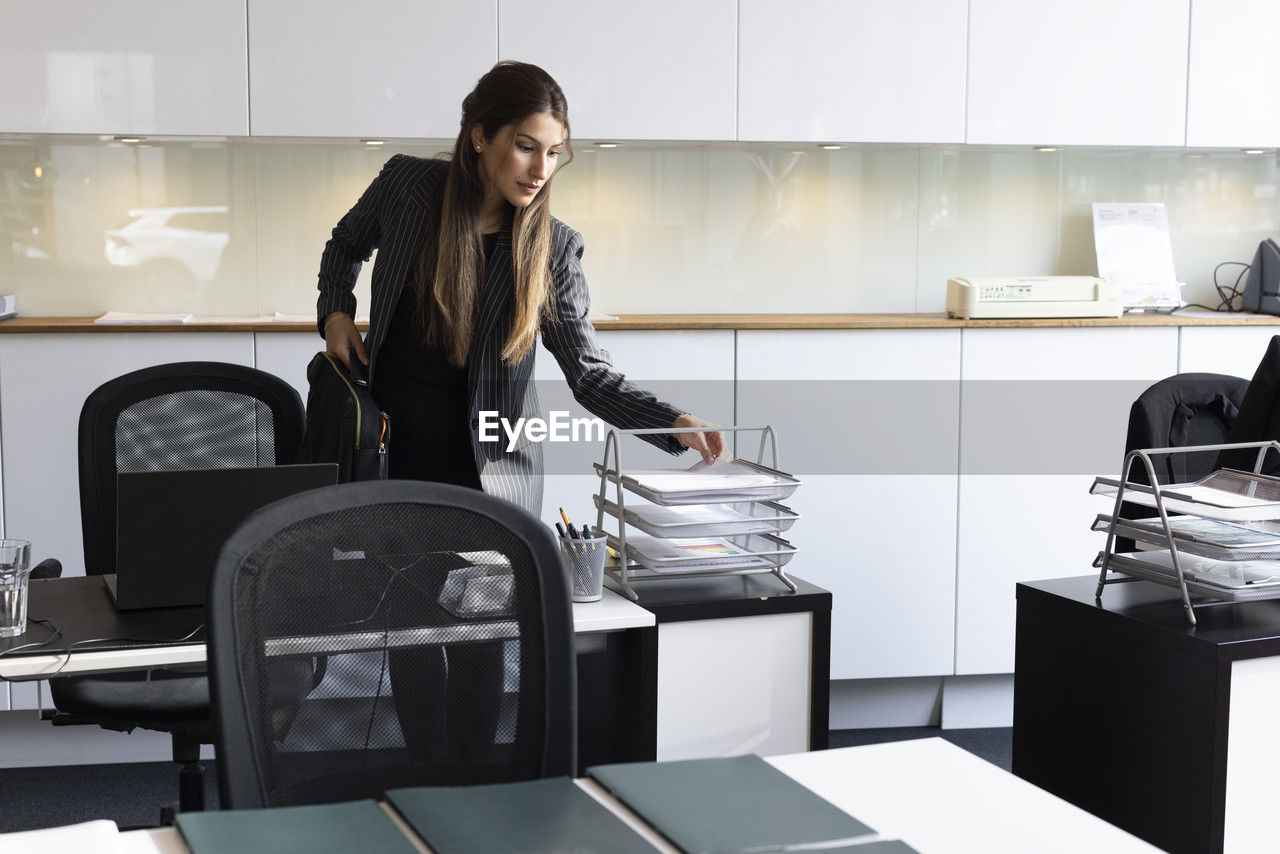 Female real estate agent arranging documents on rack in office
