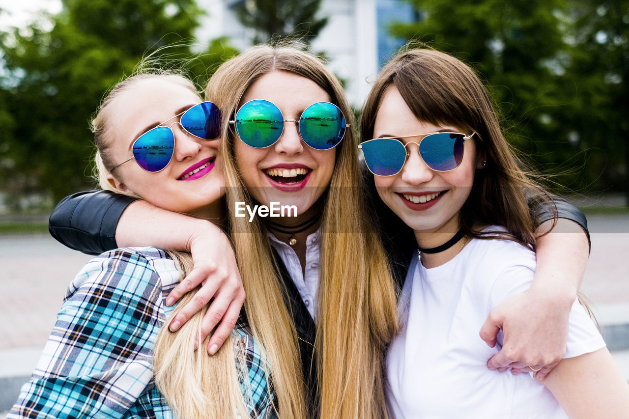 Portrait of happy female friends wearing sunglasses standing on footpath