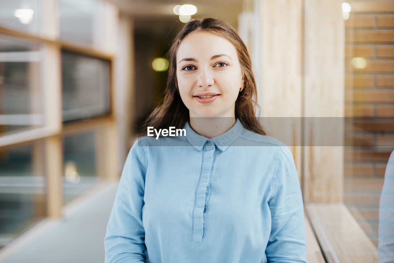 Portrait of happy young businesswoman standing at office corridor