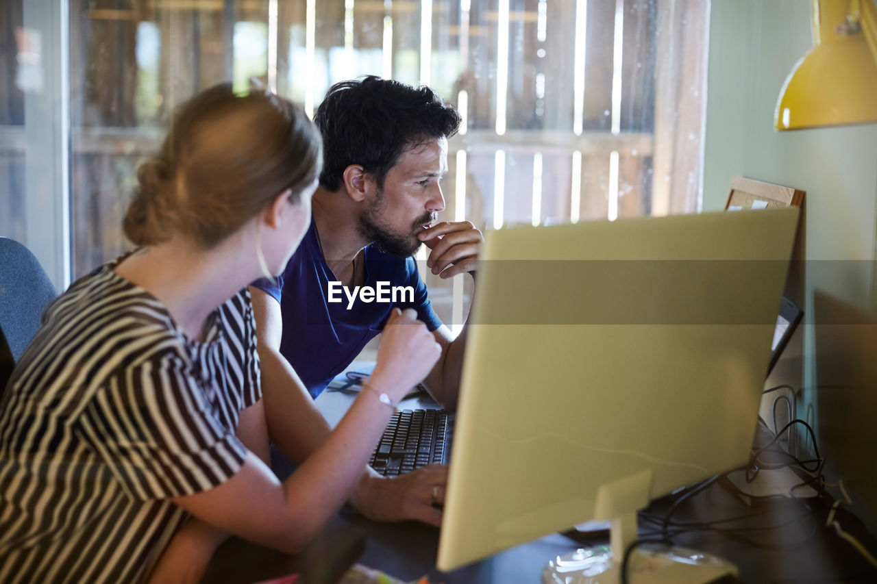 Male and female colleagues discussing at computer desk in creative office