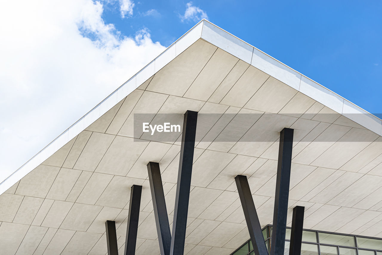 A modern concrete roof supported by steel pillars against a blue sky with clouds.