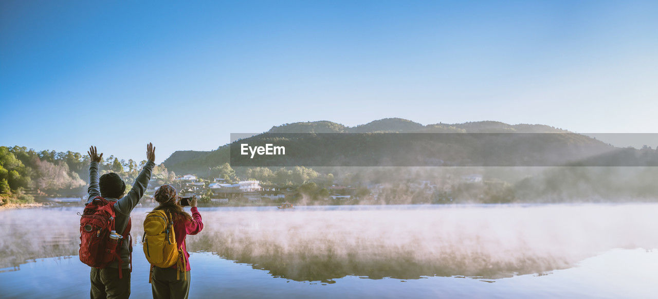 rear view of woman standing in lake against clear blue sky