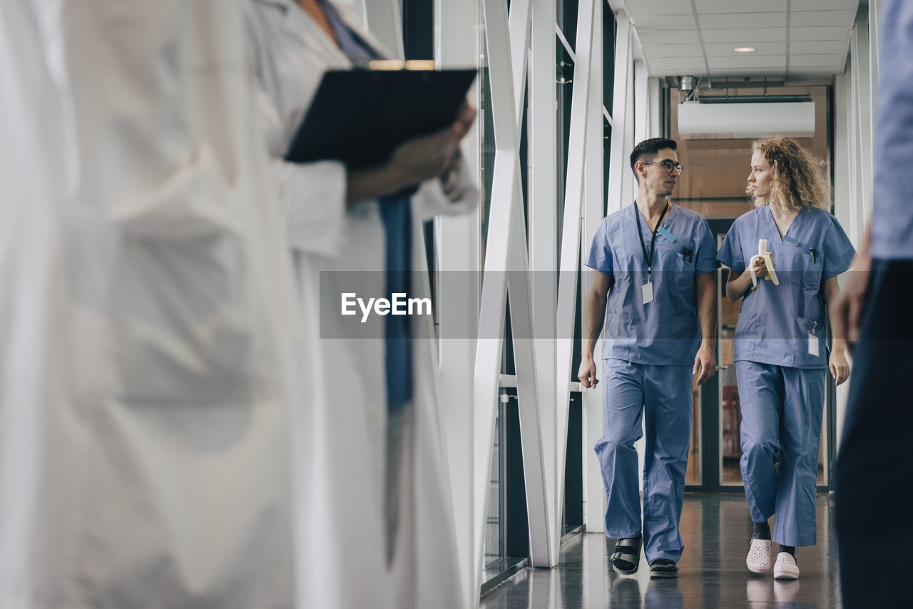 Nurse having banana talking with colleague while walking in corridor of hospital