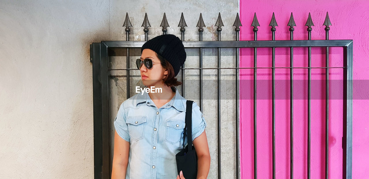 Woman wearing sunglasses standing against wall