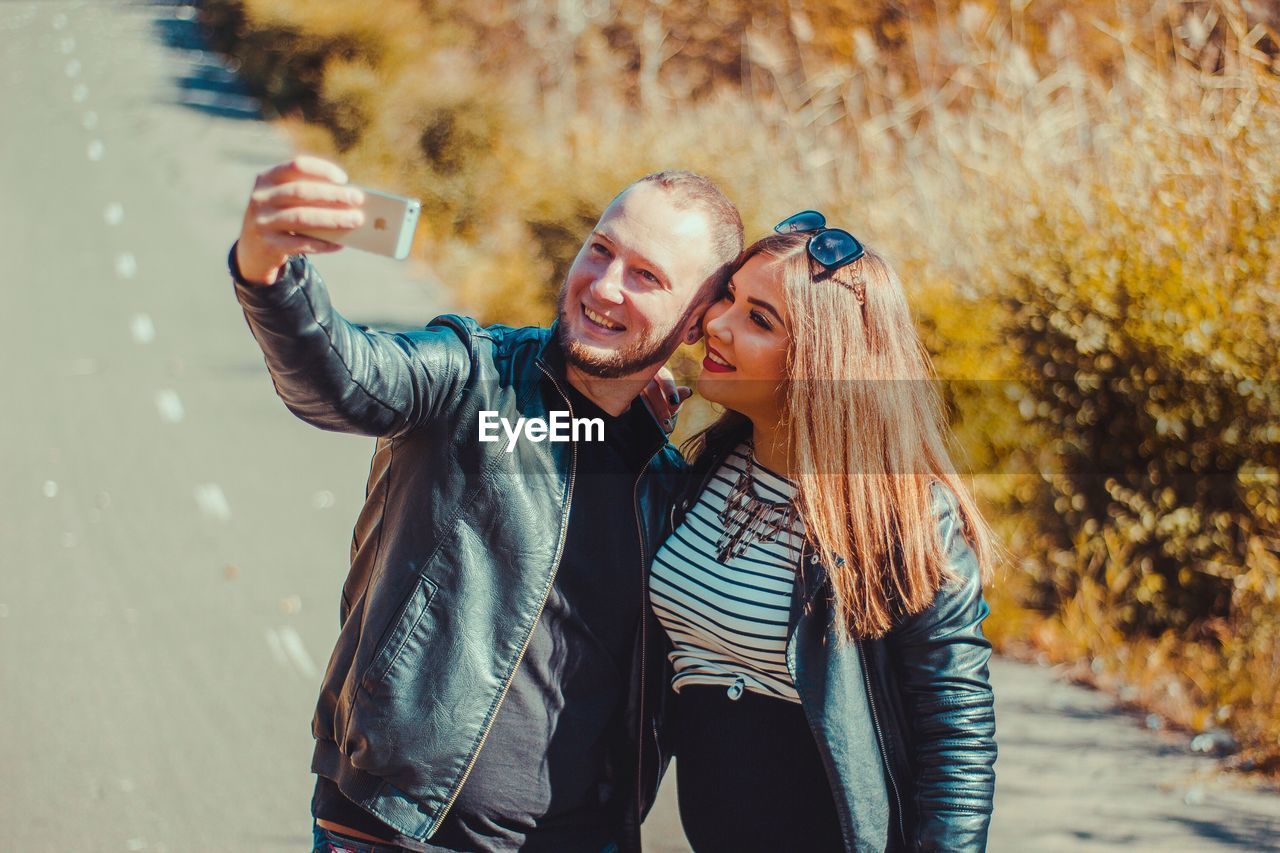 Happy couple taking selfie on road during sunny day