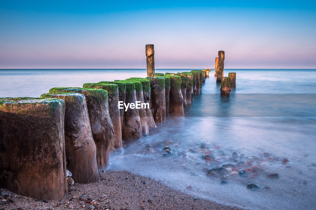 WOODEN POSTS ON SEA AGAINST SKY