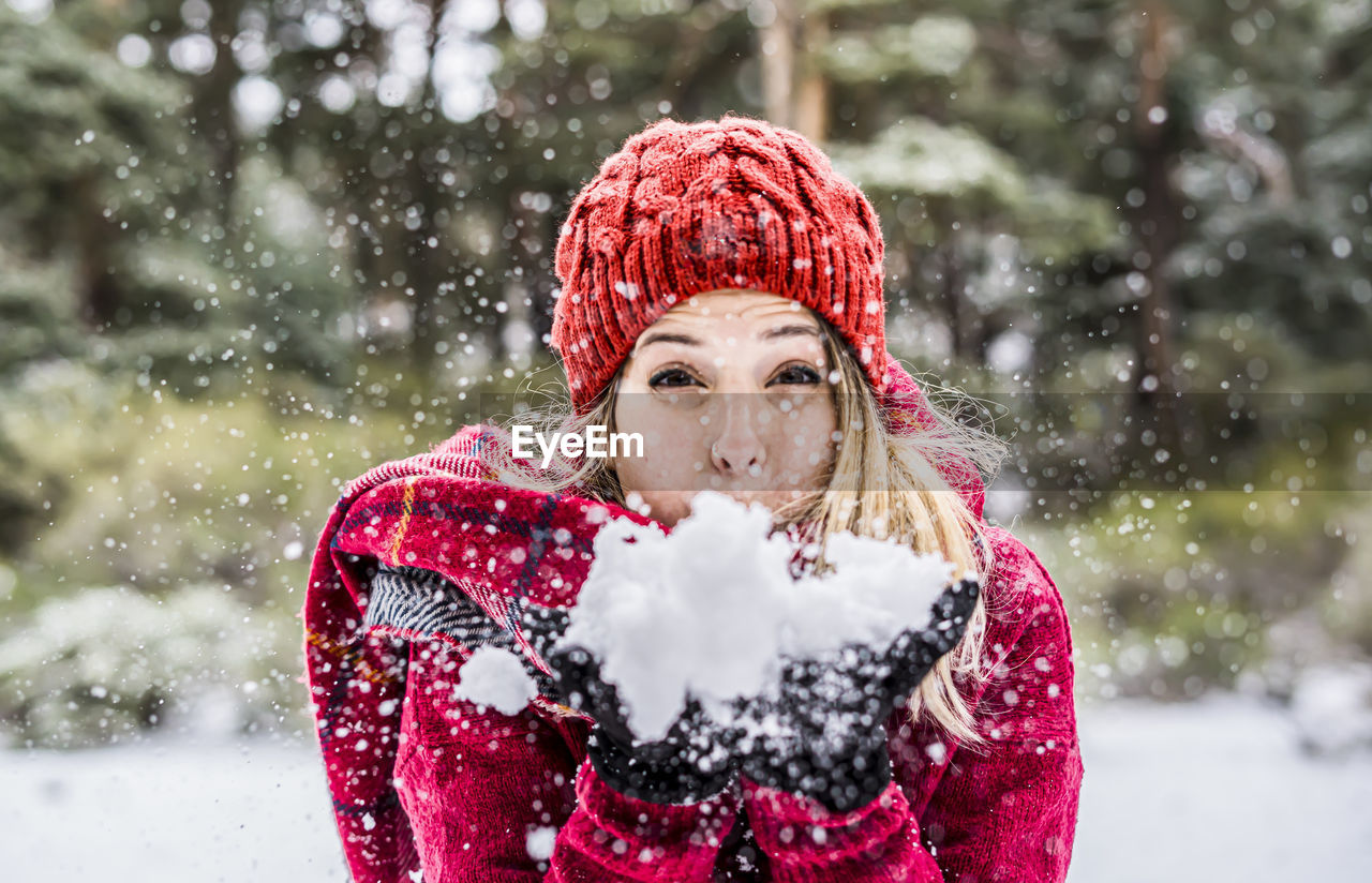 Portrait of woman blowing snow while standing outdoors during winter