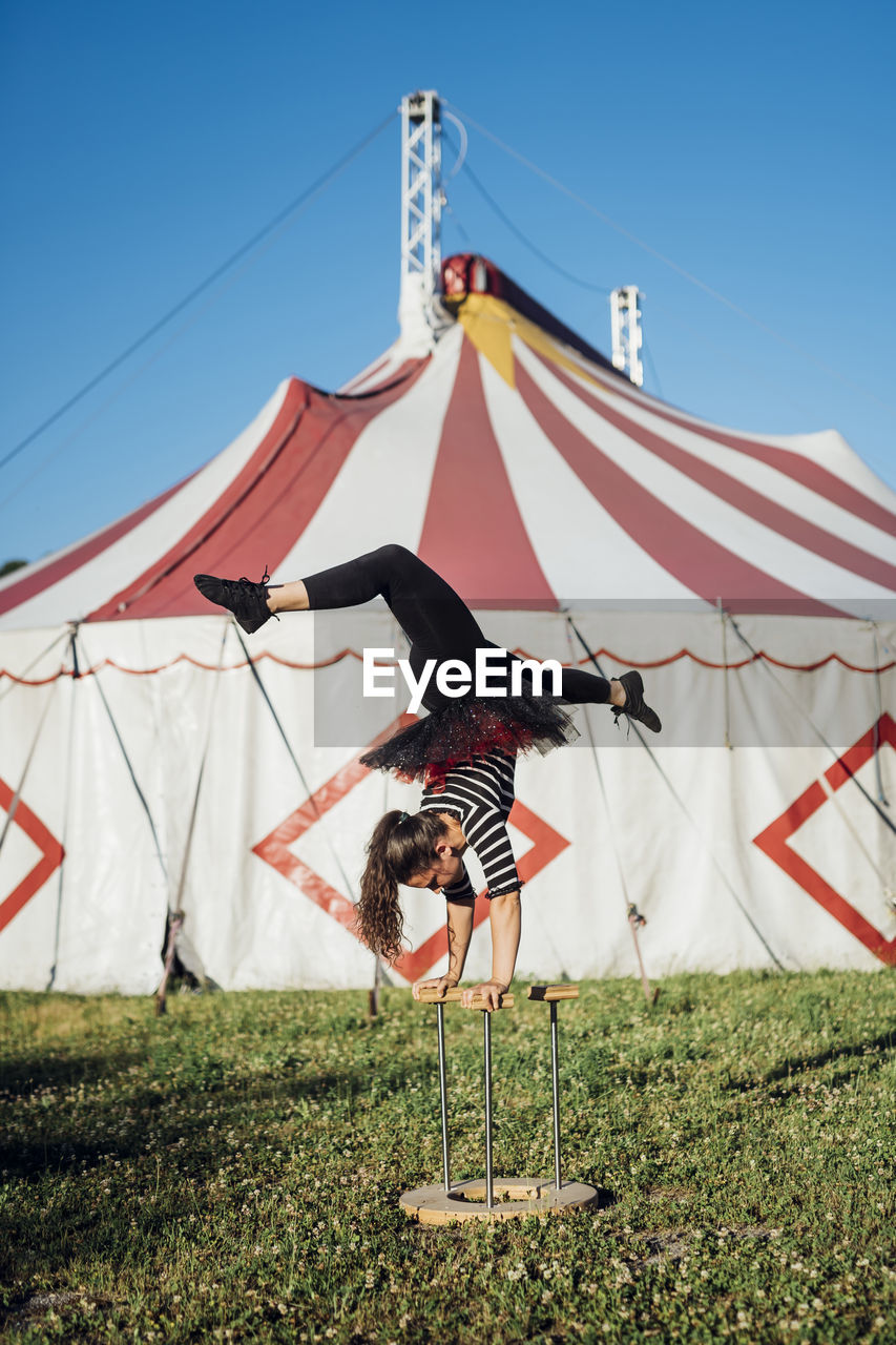 Female acrobat doing handstand on cane in front of circus tent