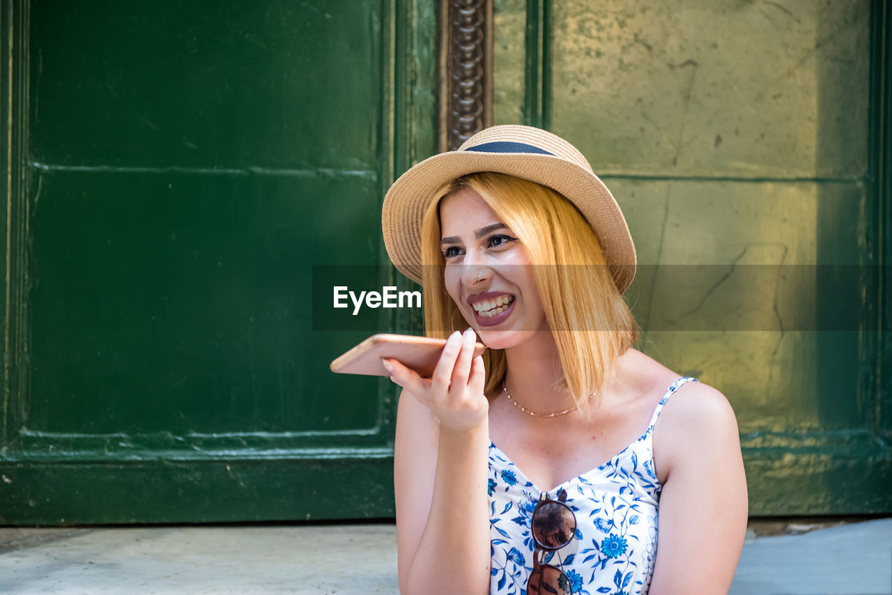 Smiling young woman wearing hat talking on phone outdoors