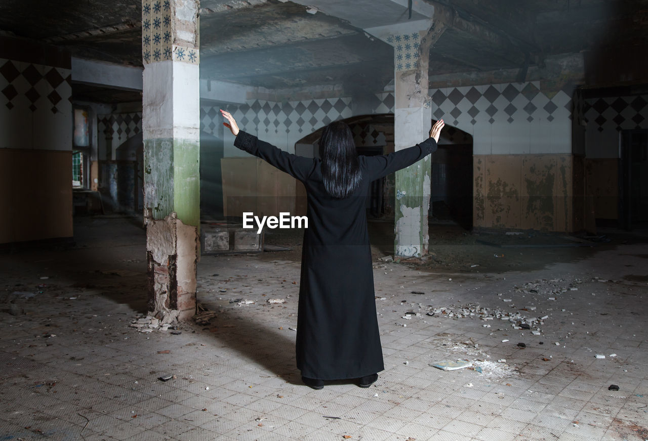 Rear view of woman with arms outstretched standing in abandoned building