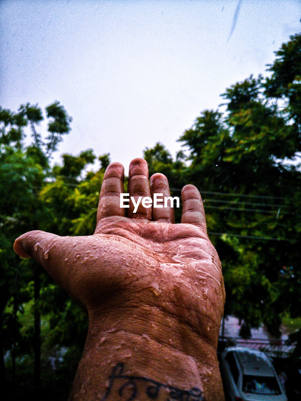 Cropped hand of man against sky during rainy season