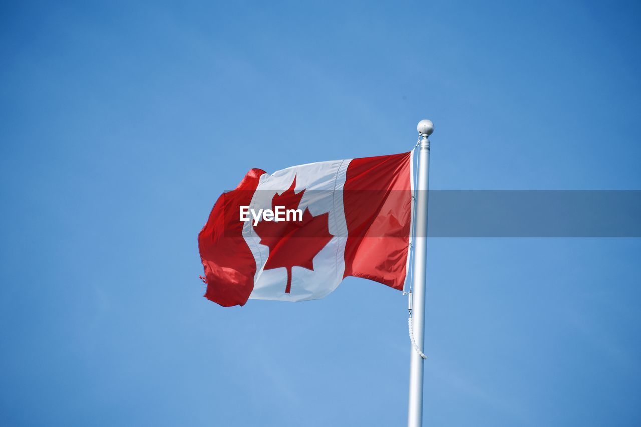 Low angle view of canadian flag against blue sky