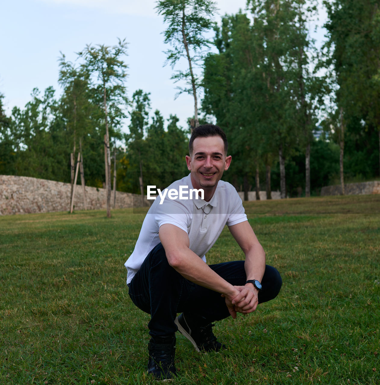 A young man posing relaxed on the grass in a park.