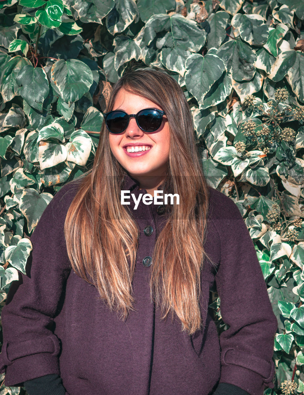 PORTRAIT OF A SMILING YOUNG WOMAN WEARING SUNGLASSES OUTDOORS