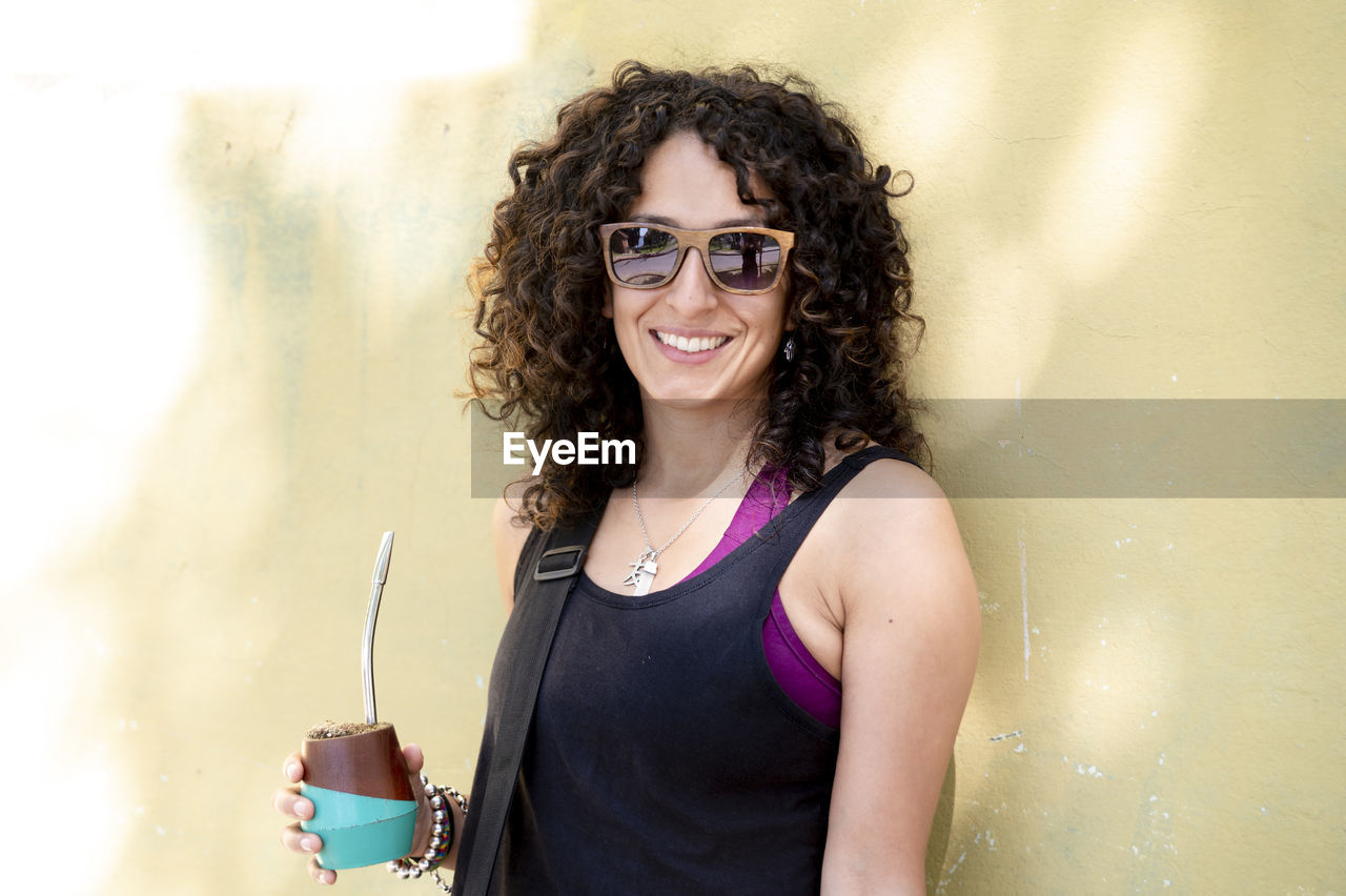 Mixed race woman smiling while drinking mate outdoors.