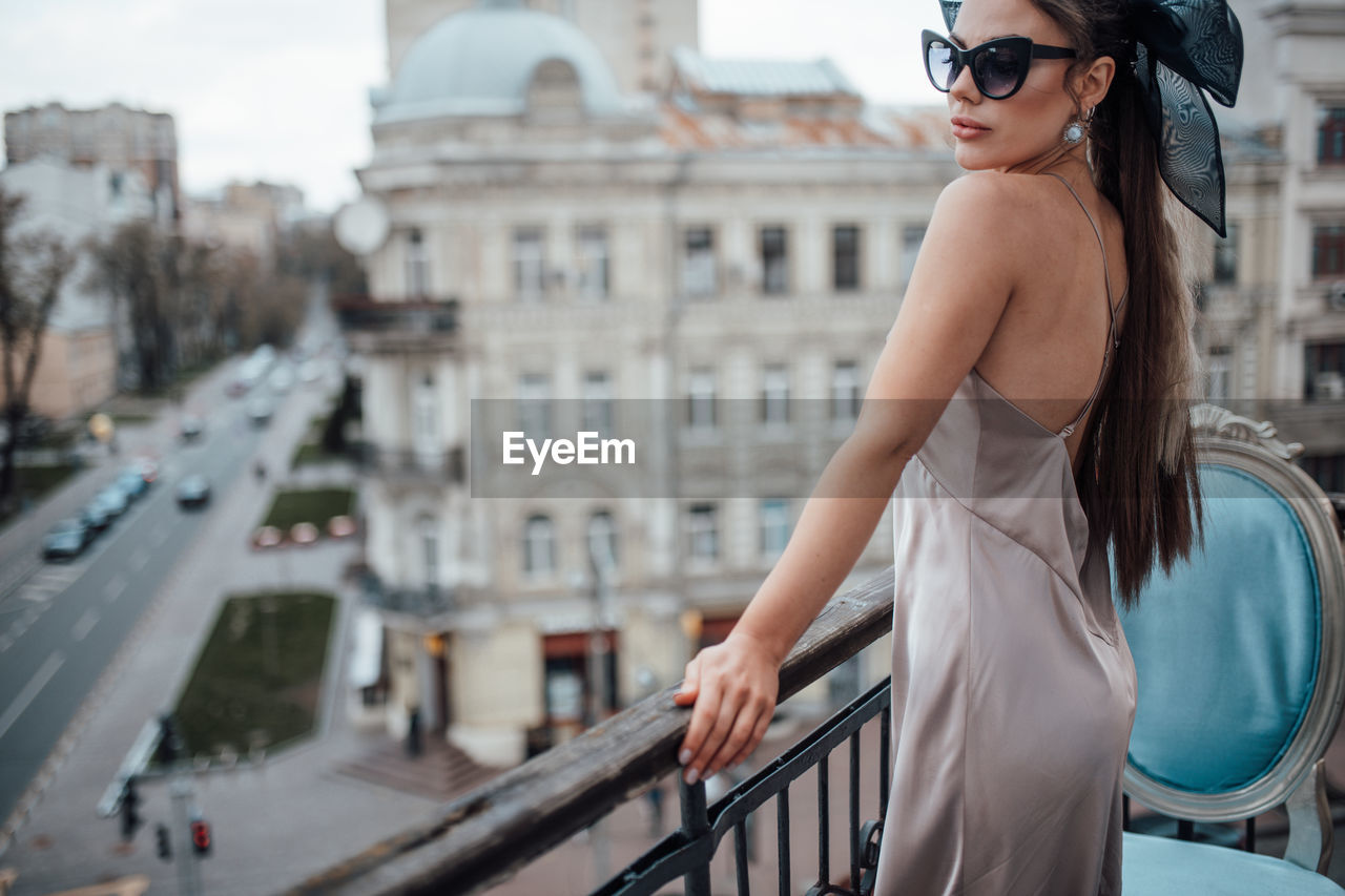 Side view of young woman standing by railing in city