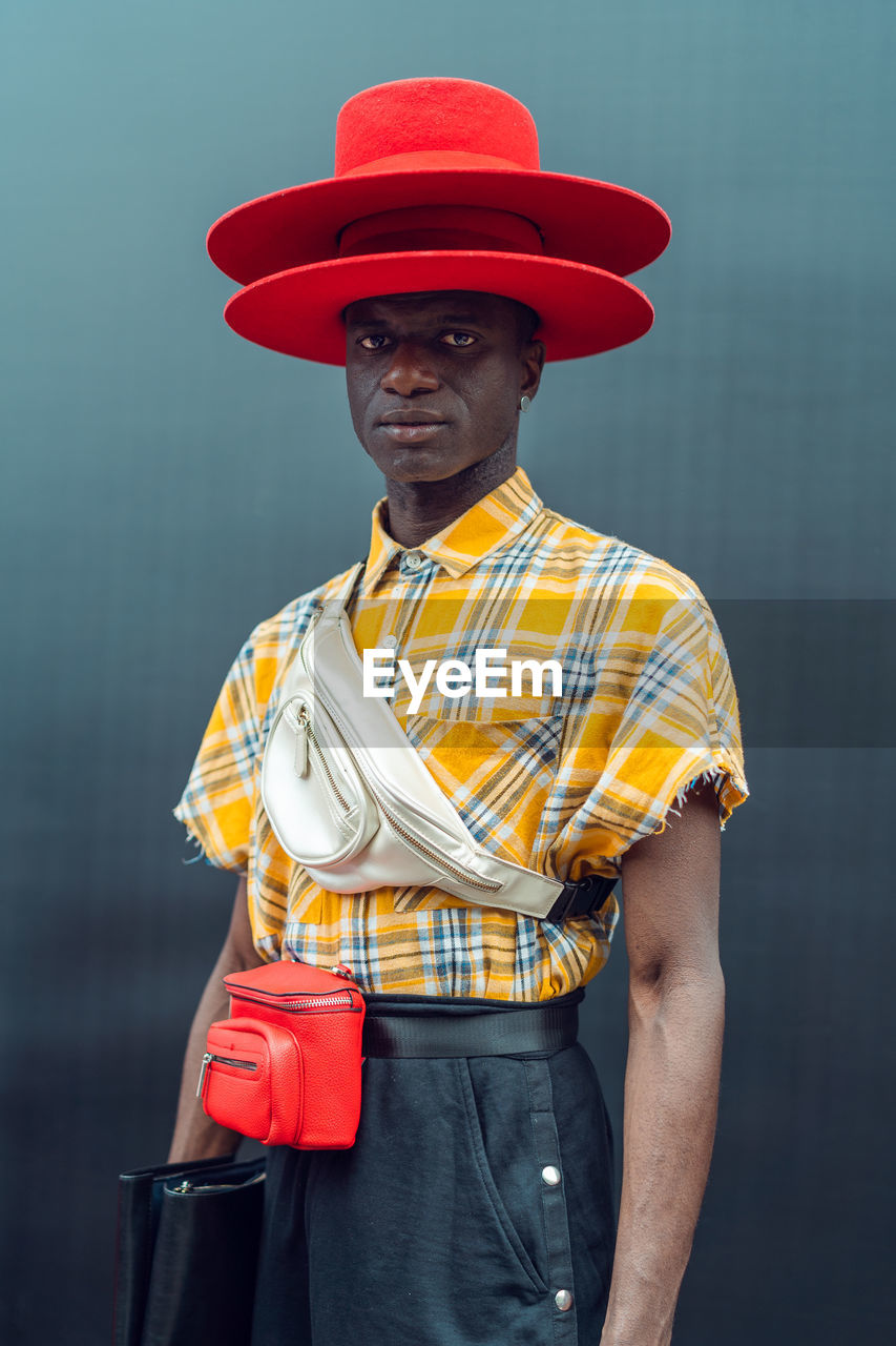 PORTRAIT OF MAN HOLDING HAT STANDING AGAINST THE WALL