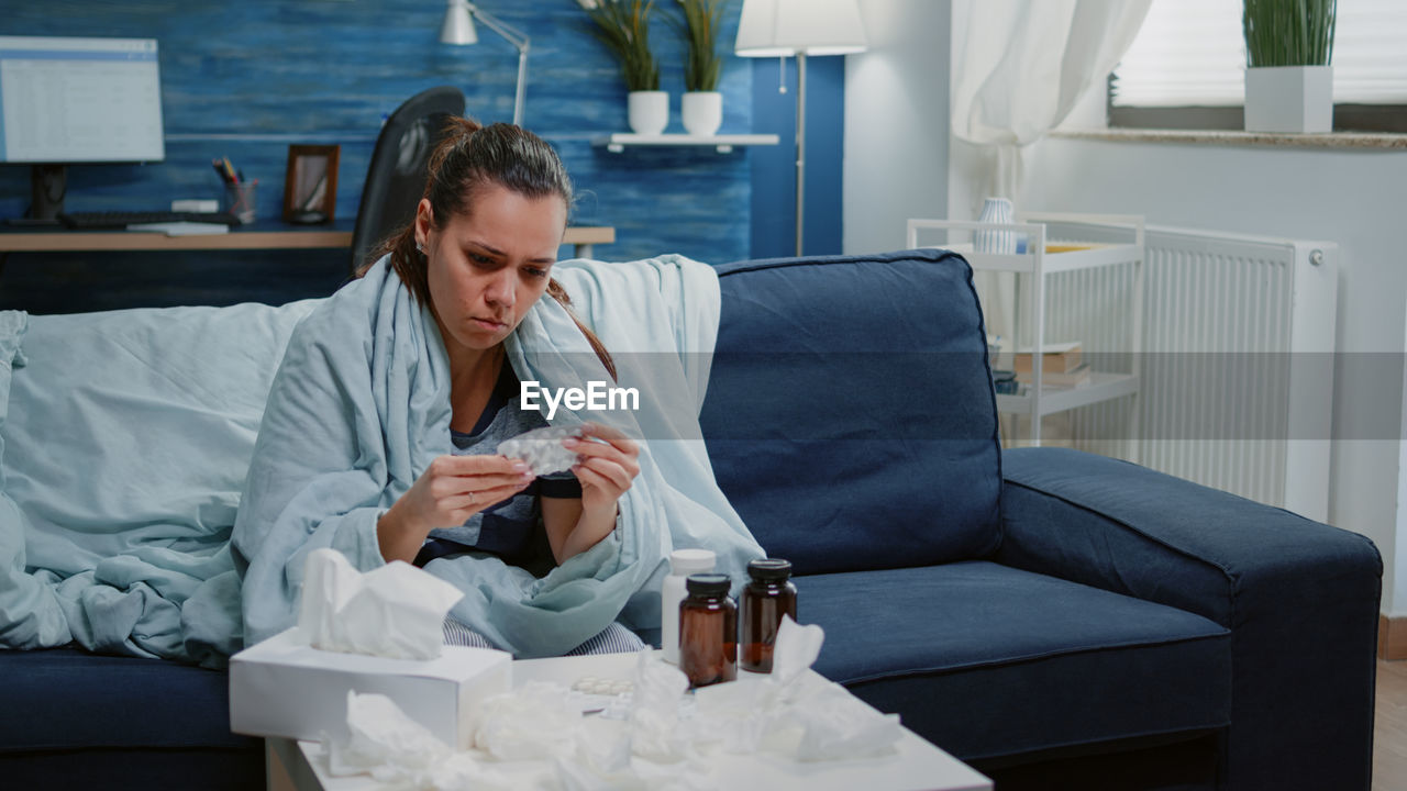 Sick woman holding medicine resting on sofa at home