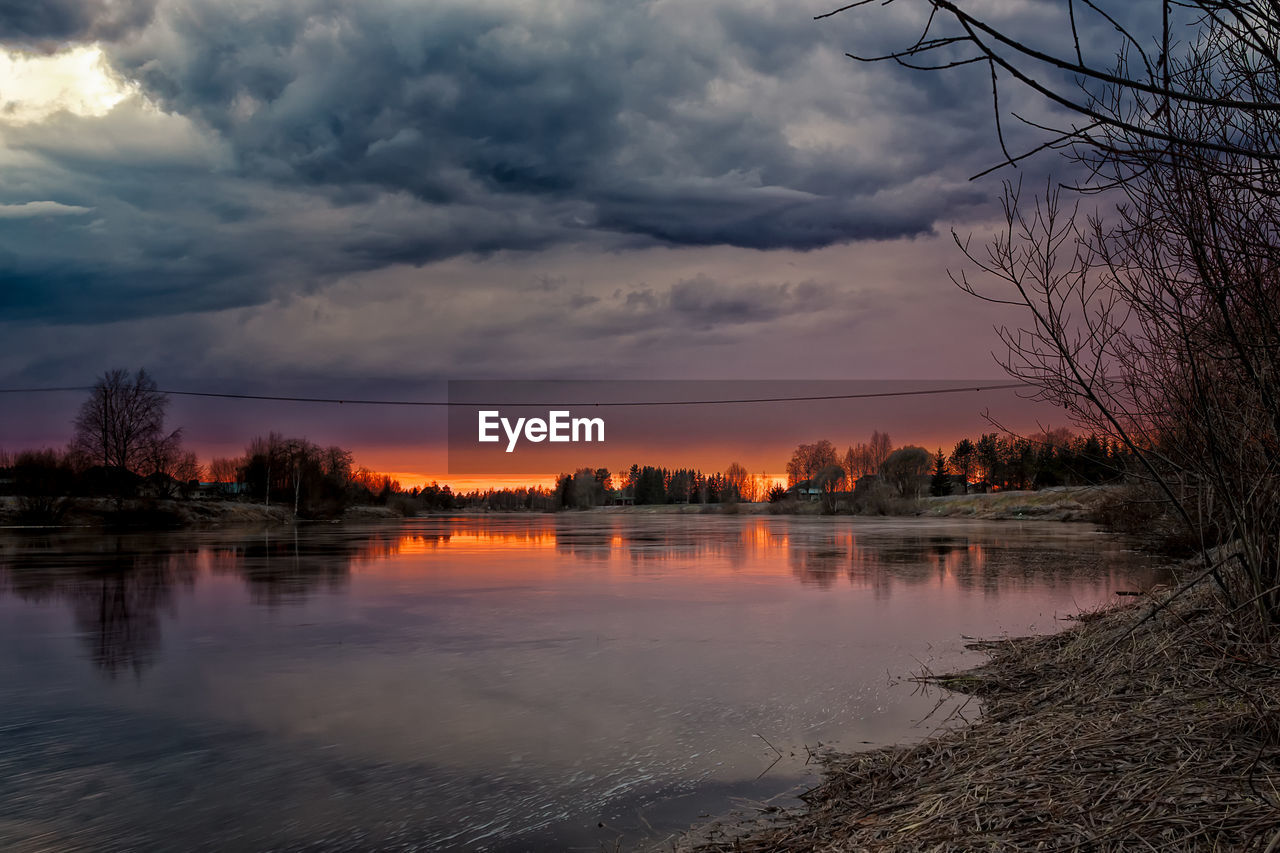 Scenic view of river against dramatic sky during sunset