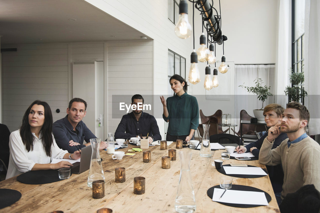 Female business professional explaining to colleagues during meeting at table in office