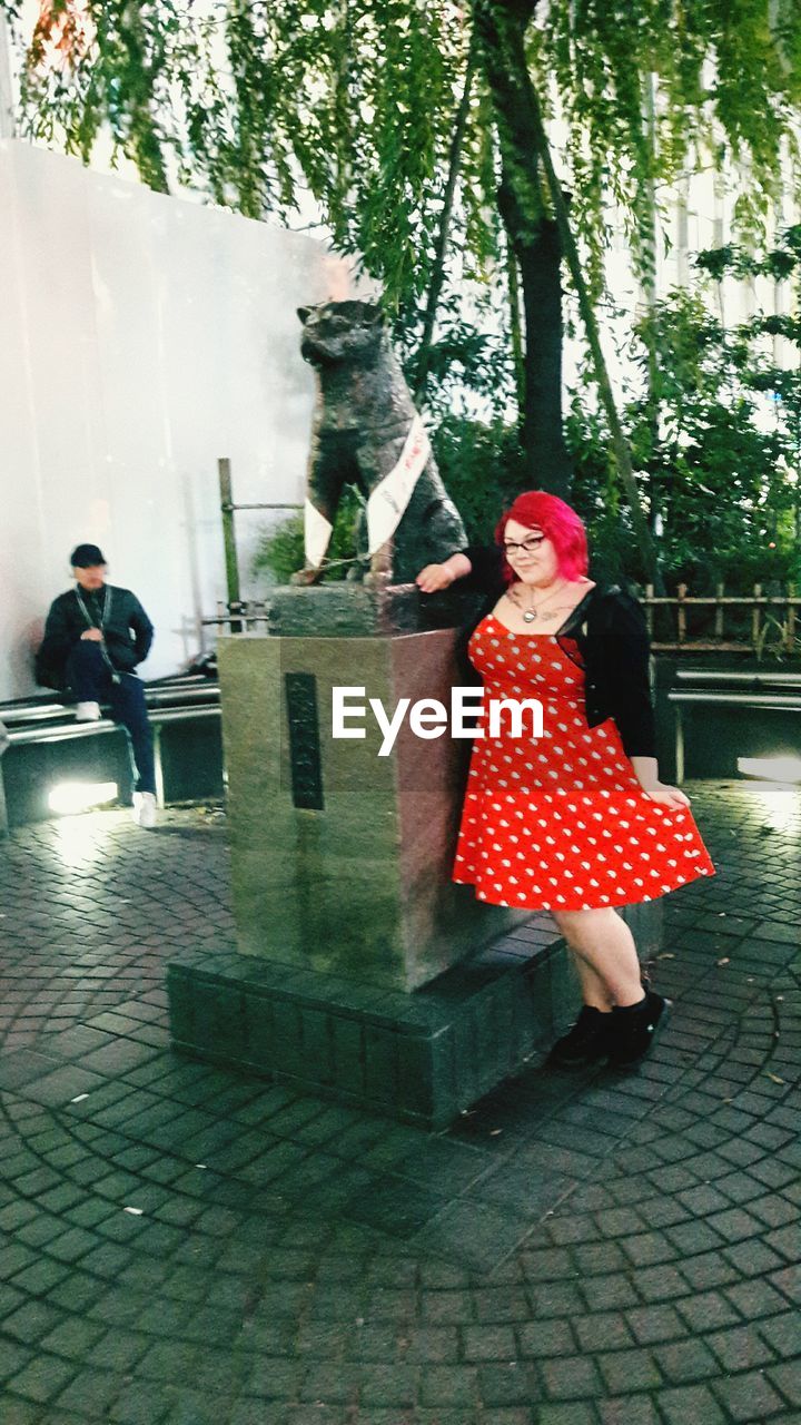 YOUNG WOMAN STANDING AGAINST TREE