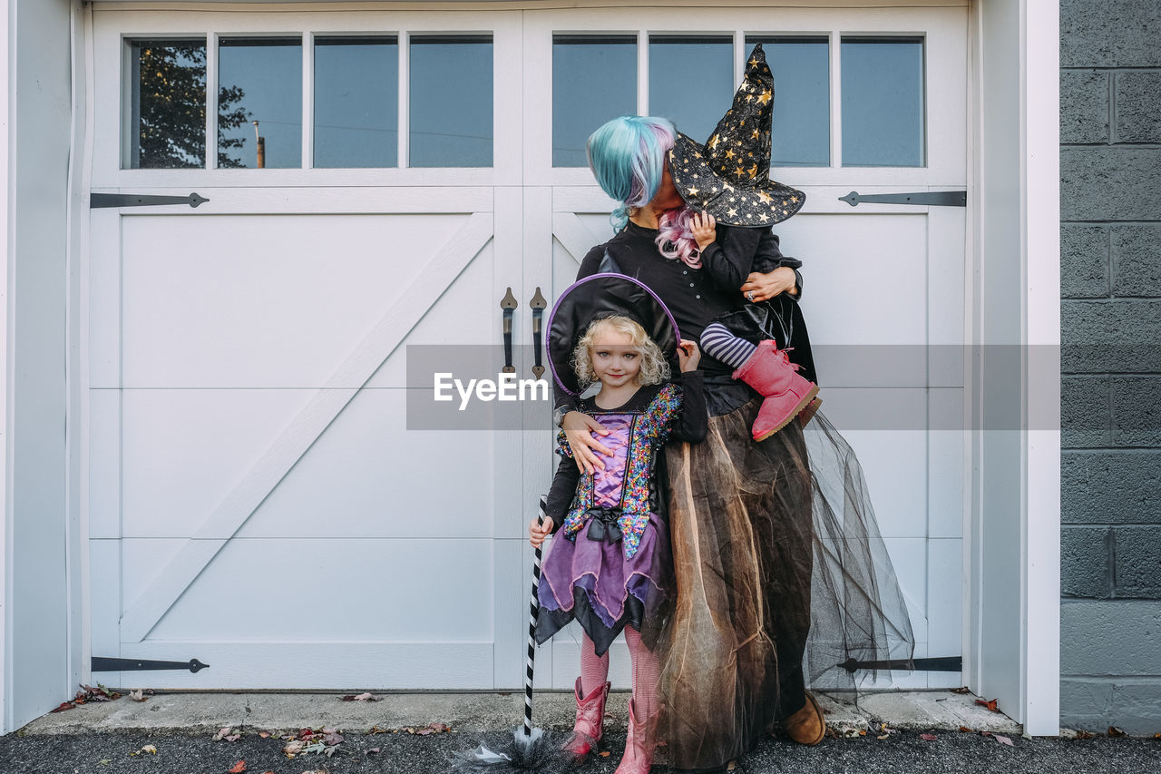 Mother with daughters in halloween costumes standing by doors