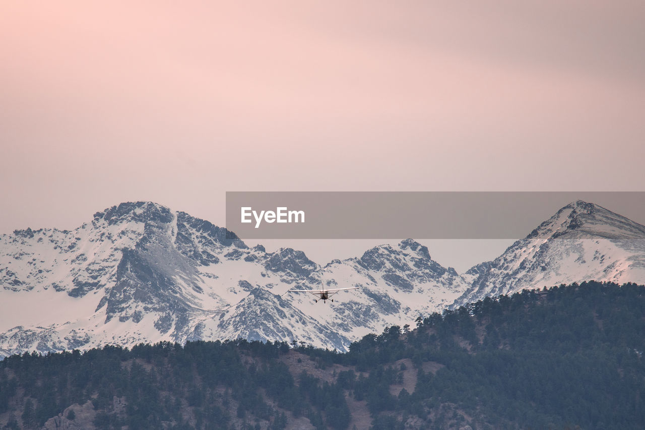 Silhouette airplane flying over snowcapped mountain against orange sky