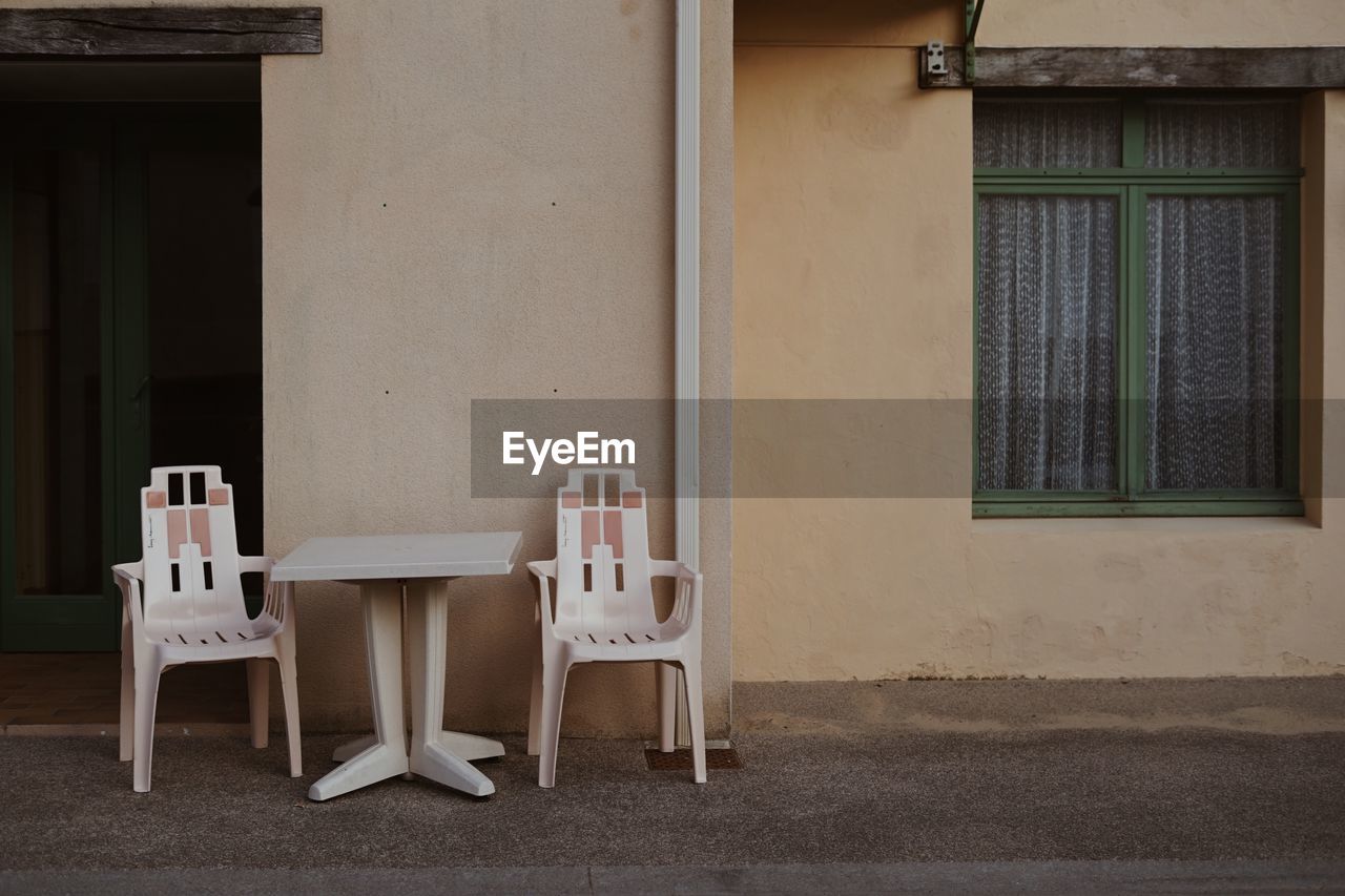 EMPTY CHAIRS AND TABLE BY WINDOW OF BUILDING