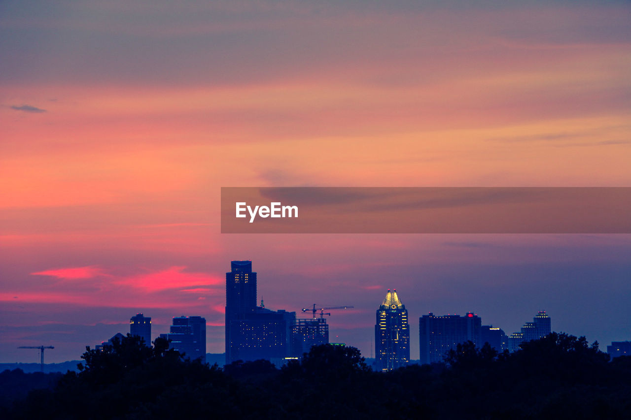 Silhouette trees against cityscape during dusk