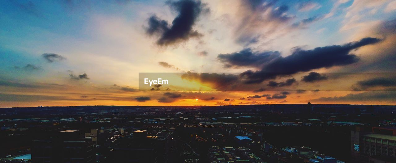 HIGH ANGLE VIEW OF ILLUMINATED CITYSCAPE AGAINST SKY DURING SUNSET