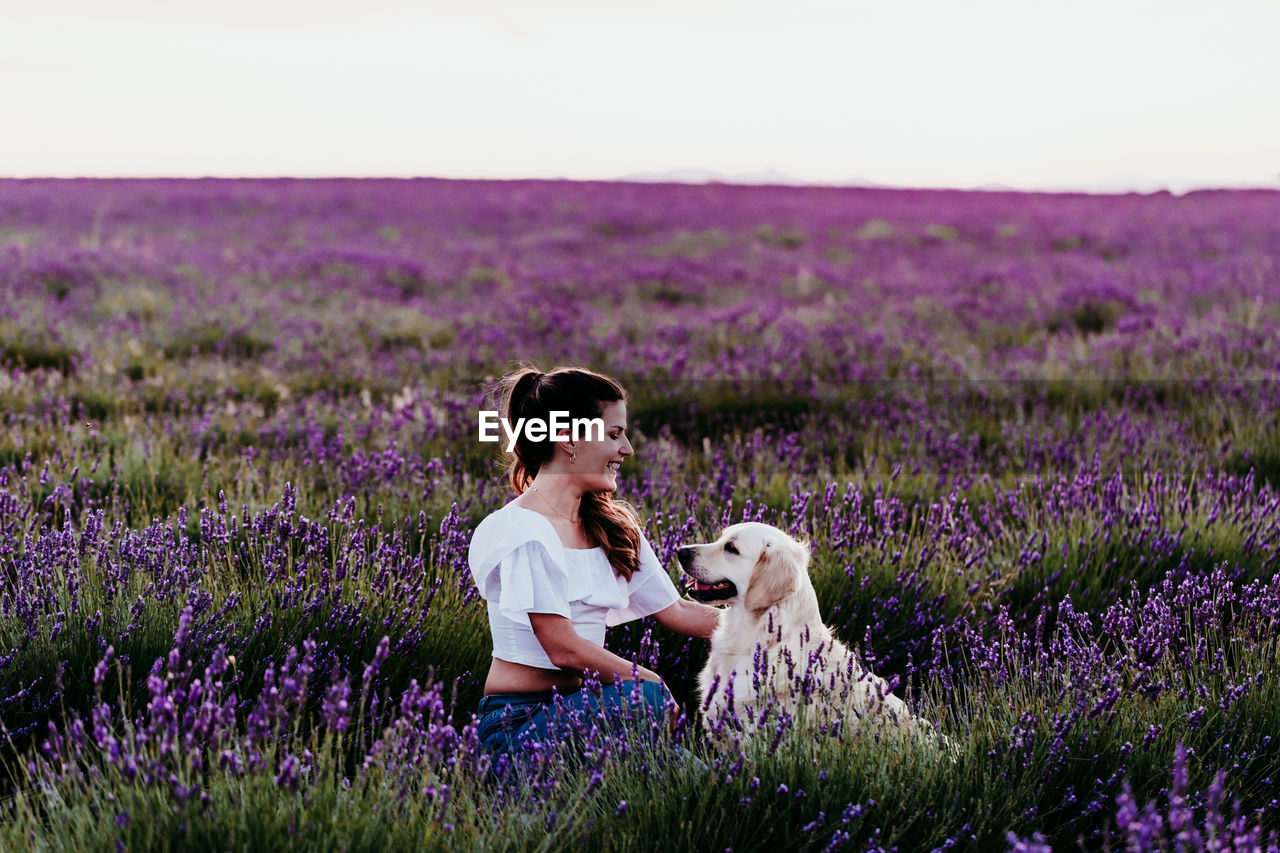 Woman sitting with dog amidst plants in lavender field