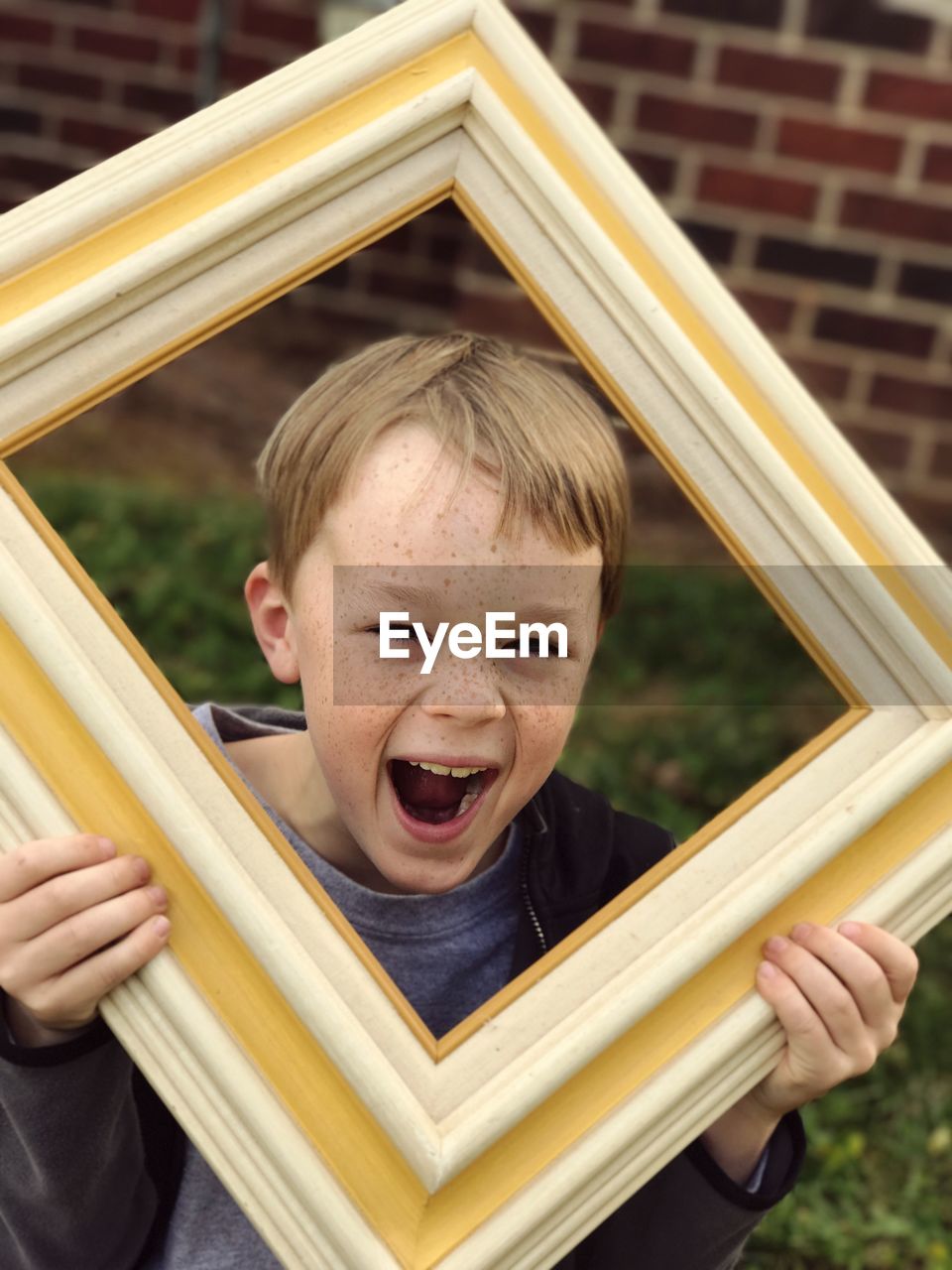 Playful boy screaming while holding picture frame at playground
