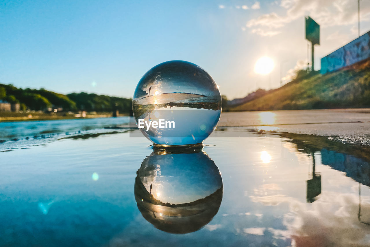 Close-up of crystal ball on puddle on road against blue sky