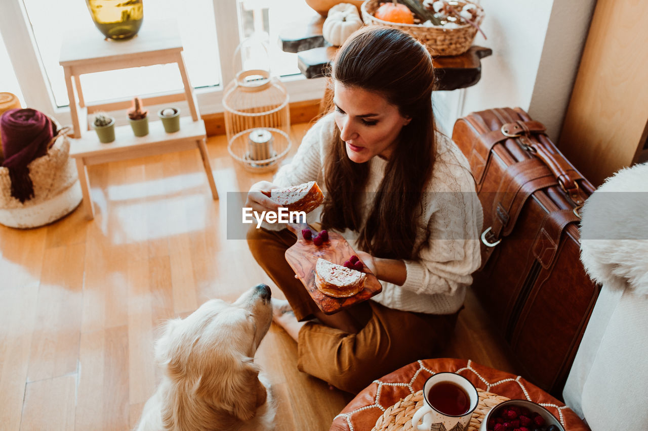 High angle view of woman feeding dog while sitting at home