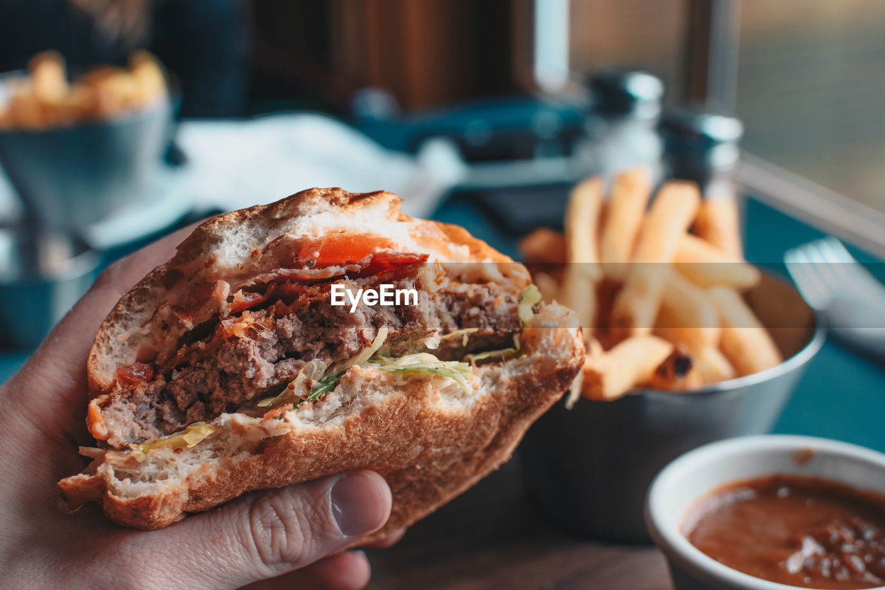 Close-up of hand holding burger in plate on table