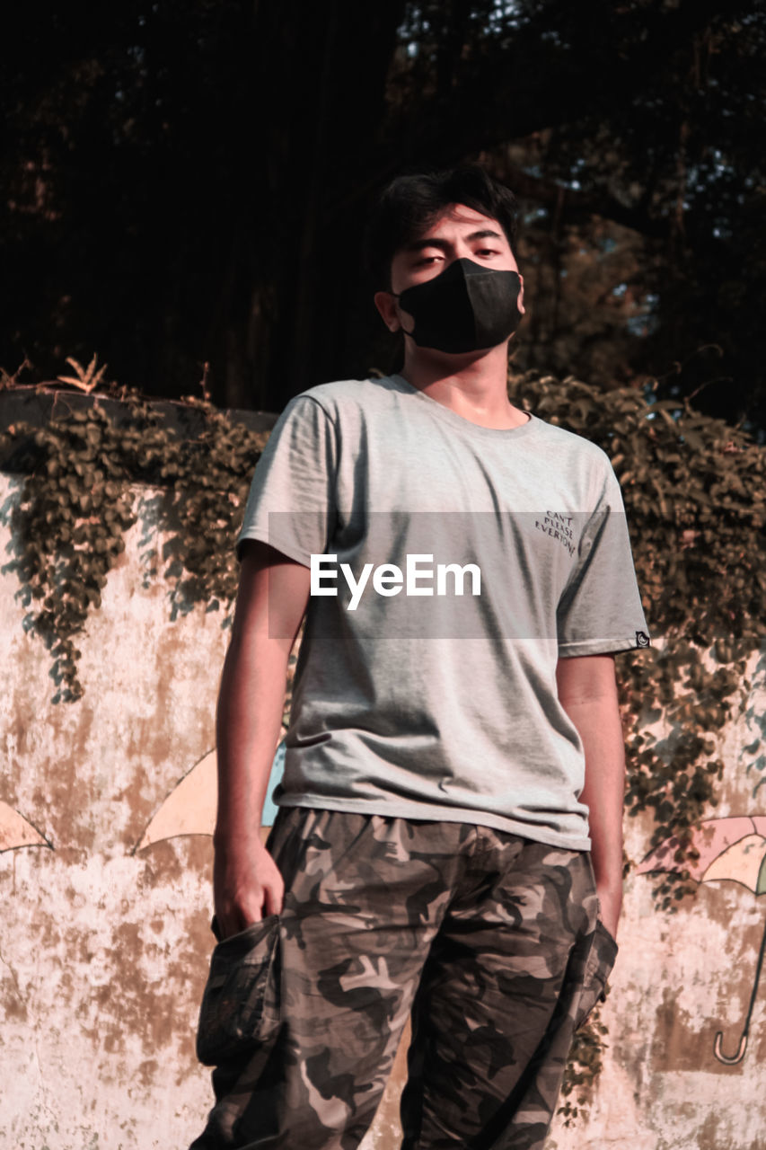 YOUNG MAN WEARING SUNGLASSES STANDING AGAINST TREE