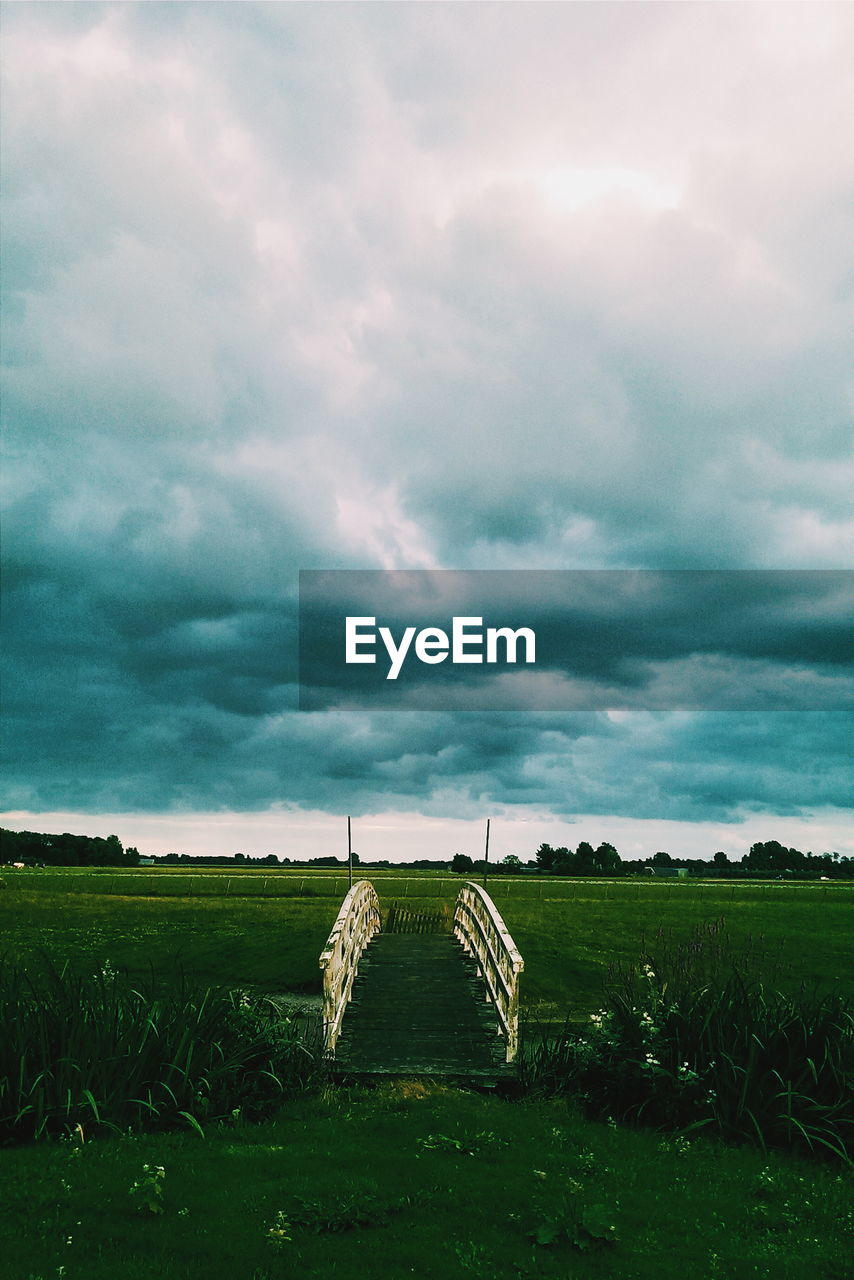 Footbridge over field against cloudy sky