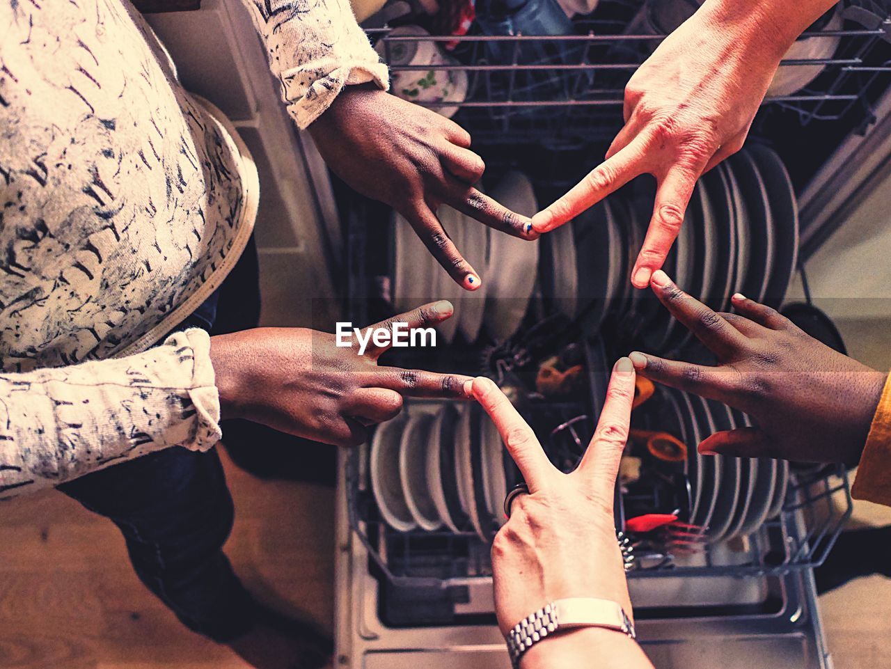 High angle view of friends making star shape with hands over plates in dishwasher