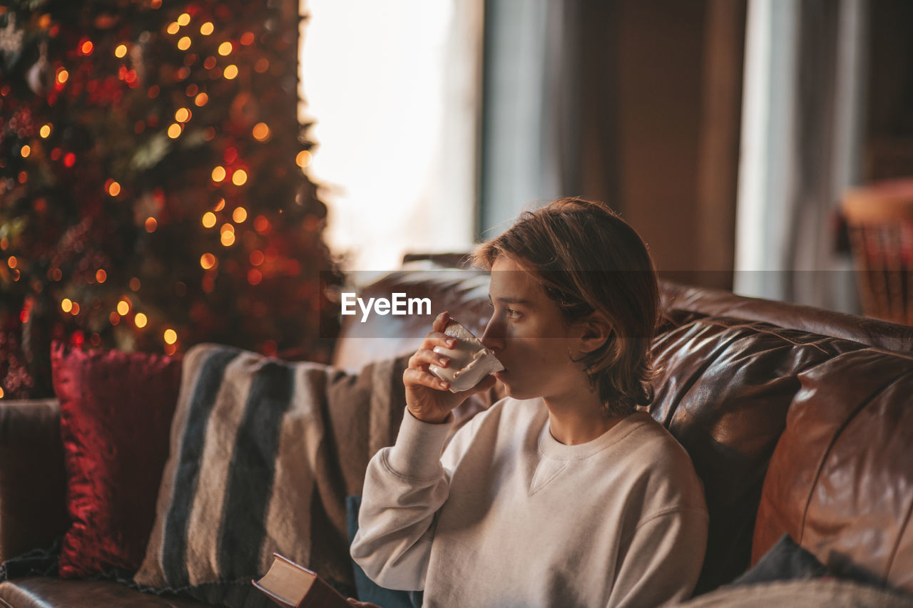 Portrait of candid authentic smiling handsome boy teenager using mobile phone at xmas home interior