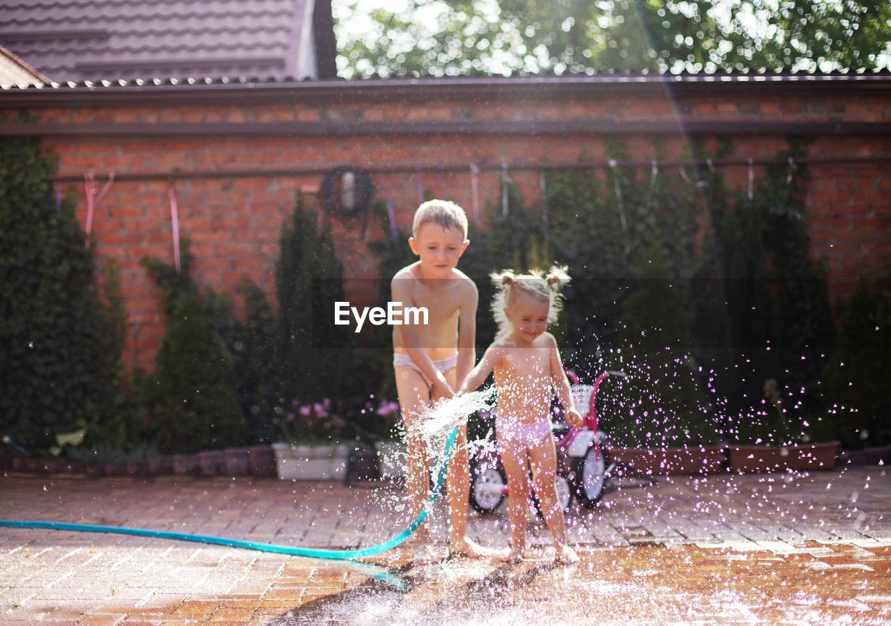 Sibling playing with water hose outdoors