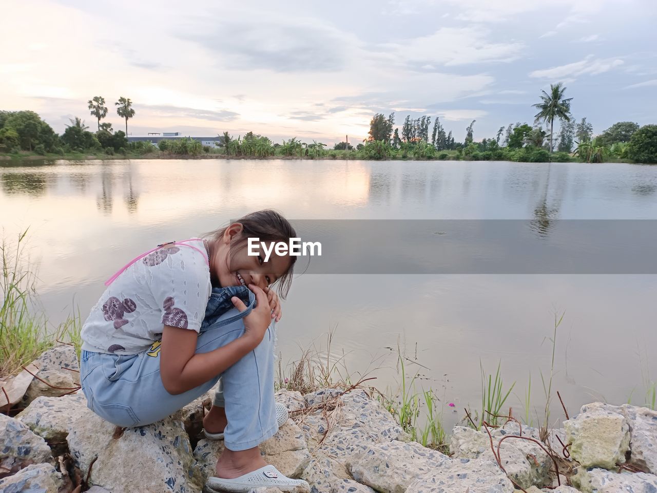 WOMAN SITTING ON LAKE AGAINST SKY