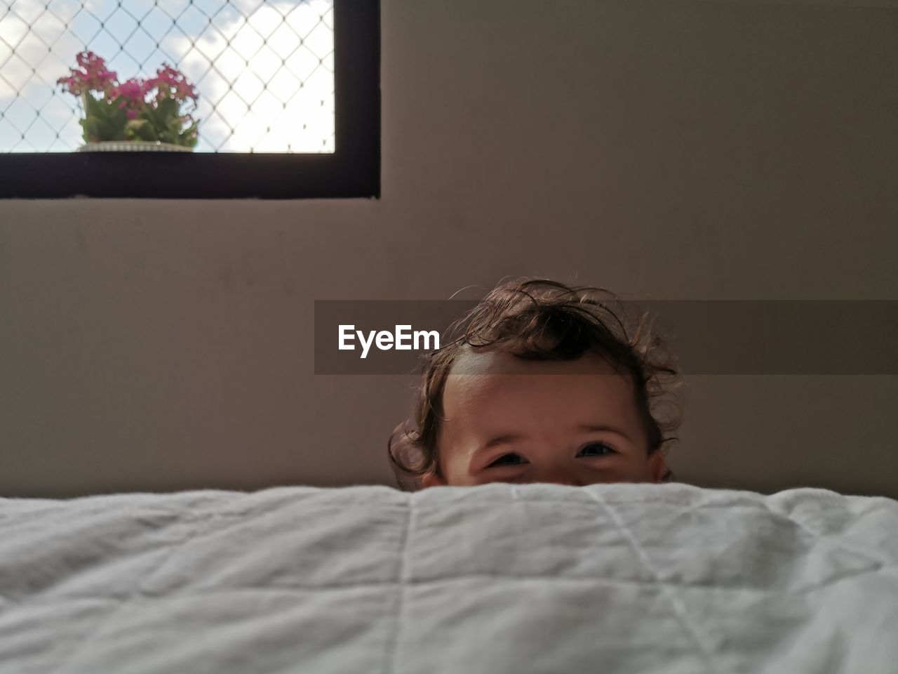 Portrait of cute girl hiding behind bed at home