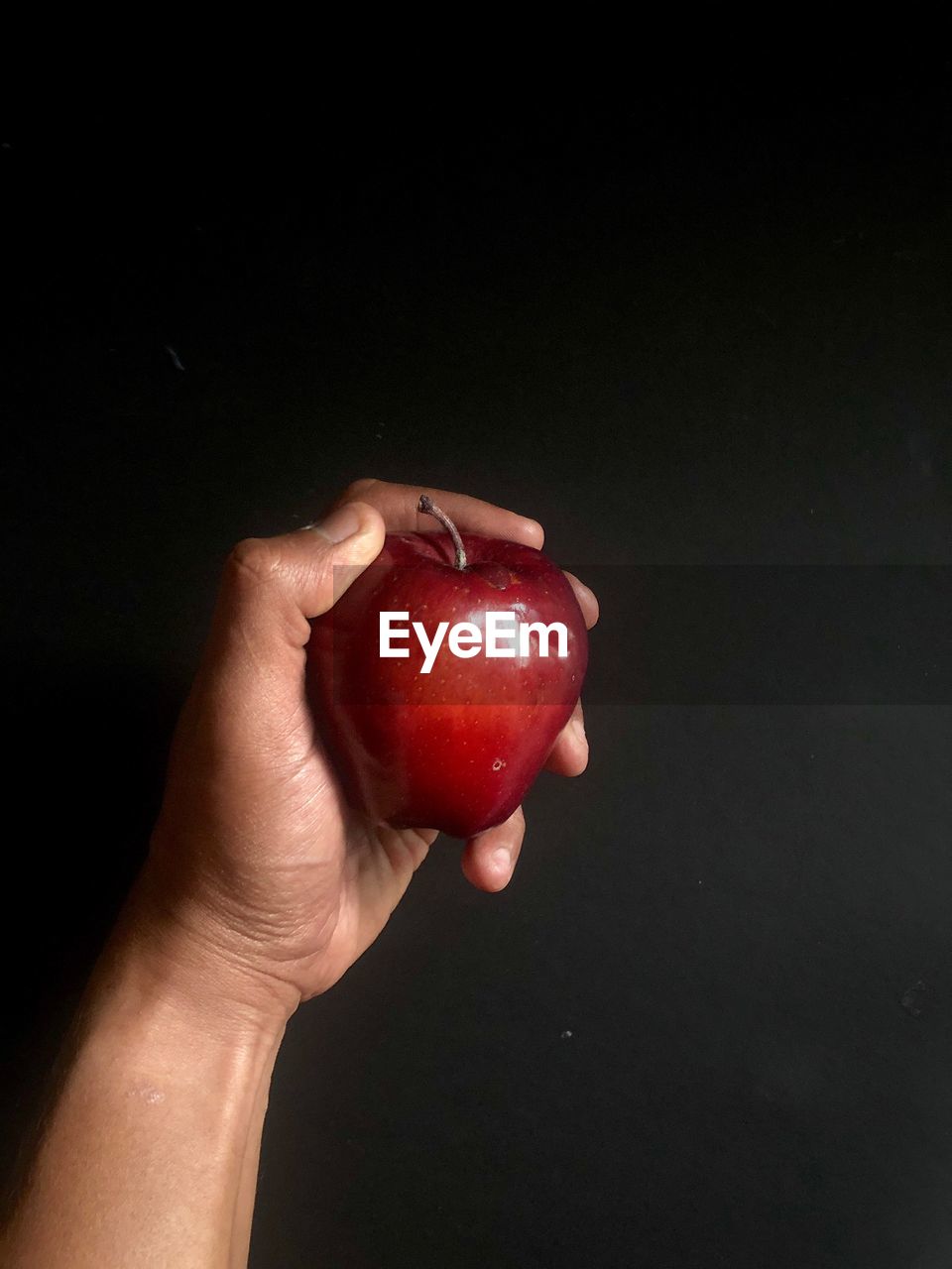 Close-up of hand holding red apple against black background