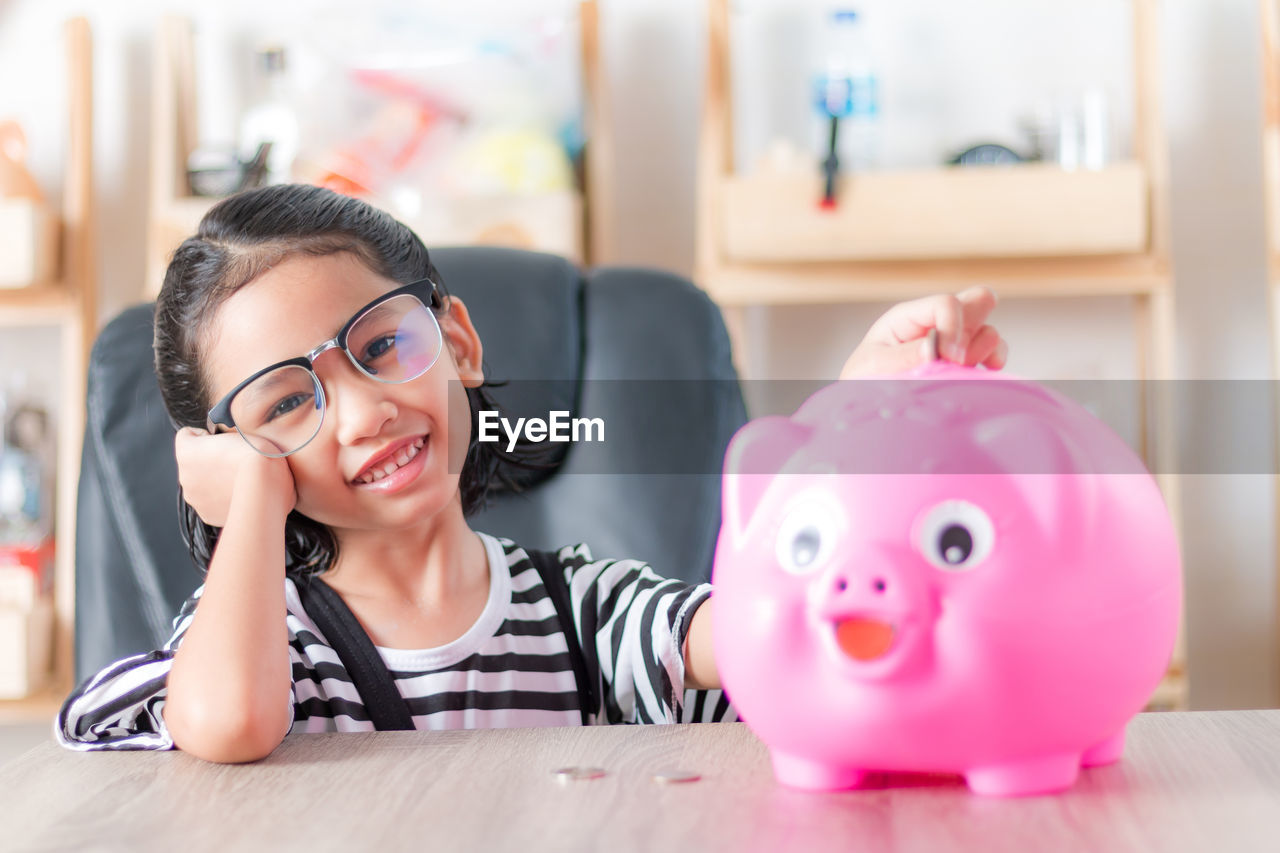 Portrait of girl putting coin in piggy bank at home