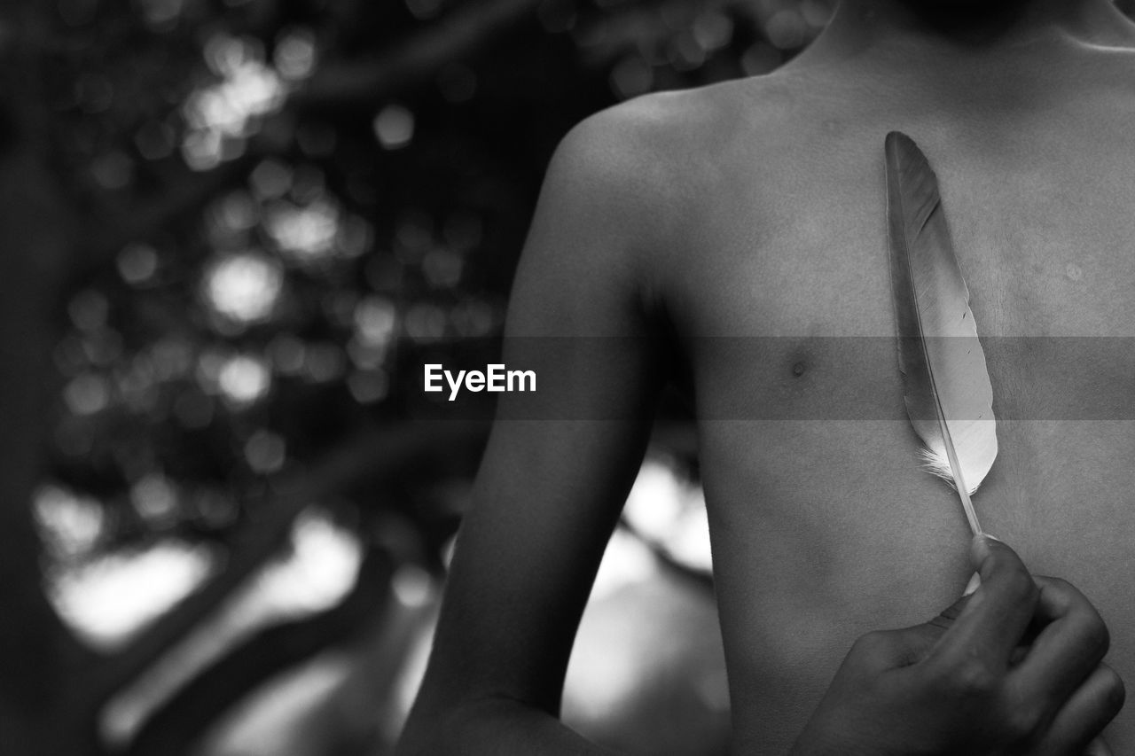 Midsection of shirtless boy holding feather