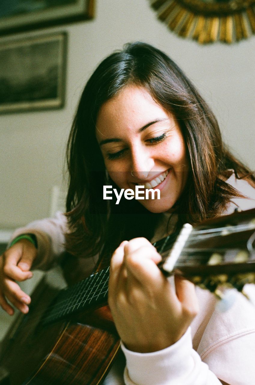 Smiling young woman playing guitar while sitting at home