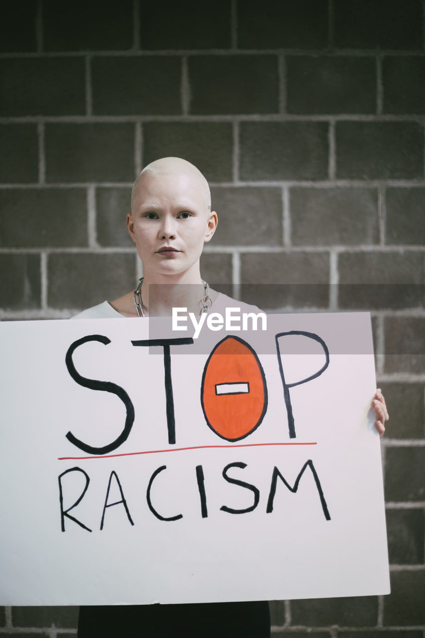 Young female protestor with stop racism sign against wall